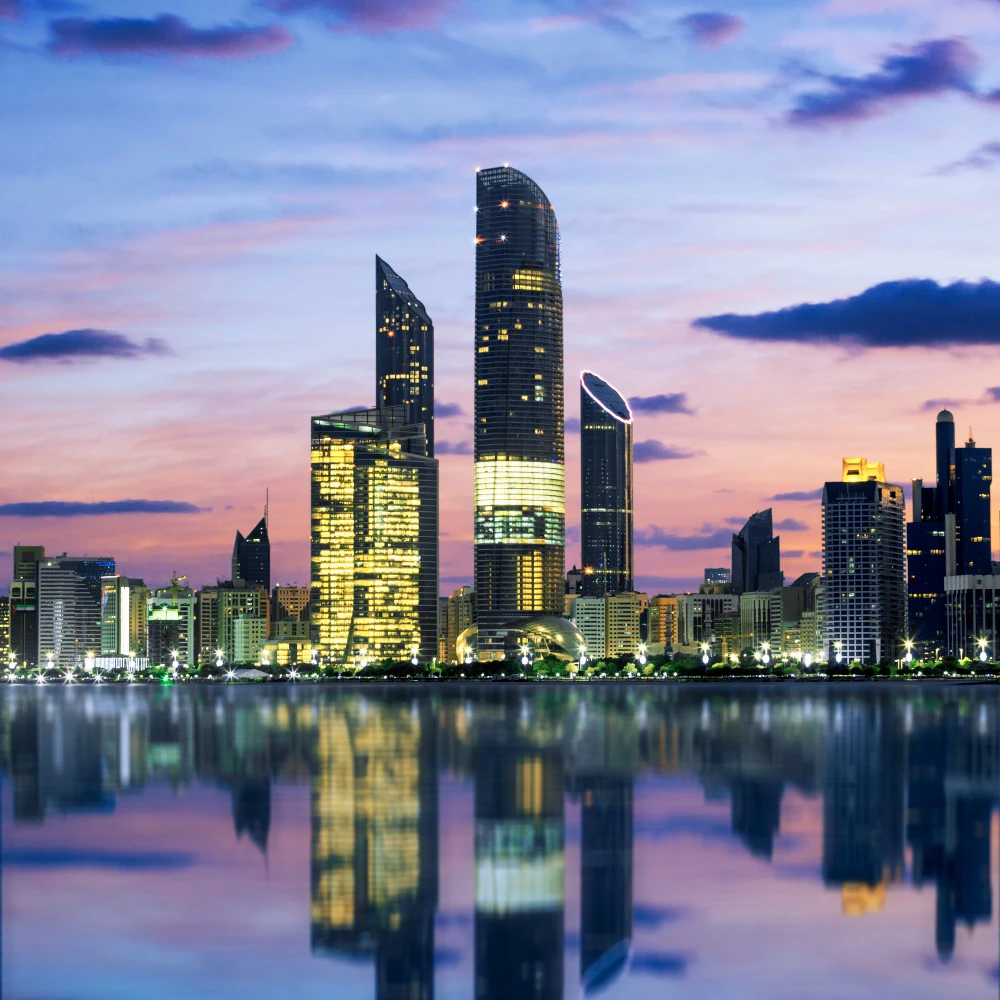 גורדי שחקים מוארים עם השתקפות במים בשעת ערב – השקעות נדל"ן יוקרתי ונכסים מודרניים על קו המים